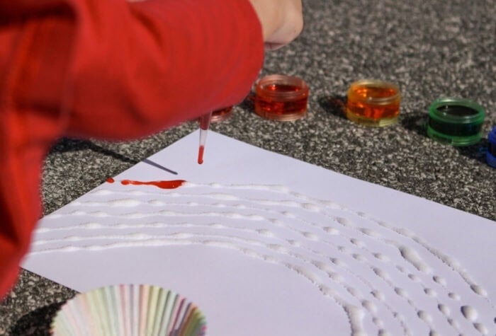 Bright Rainbow Salt Painting for Preschoolers 11 child's hand using a clear pipette to drip colored water onto a raised salt art project
