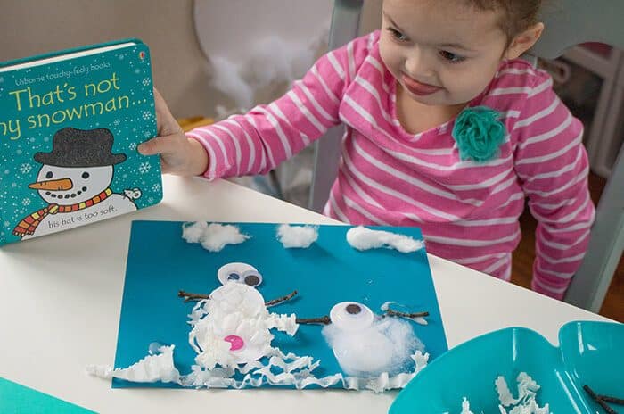 child looking at her finished snowman craft and holding a snowman book.