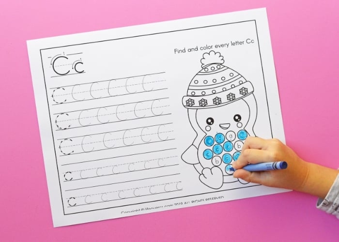 overhead picture of a child coloring in the letter "c" on a penguin themed alphabet worksheet.