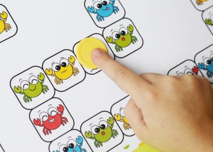 child's finger moving a game piece on a printable crab board game
