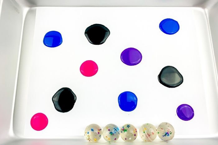bouncy balls in a paper lined pan with blue, black, purple and red paint in it for the galaxy process art activity.