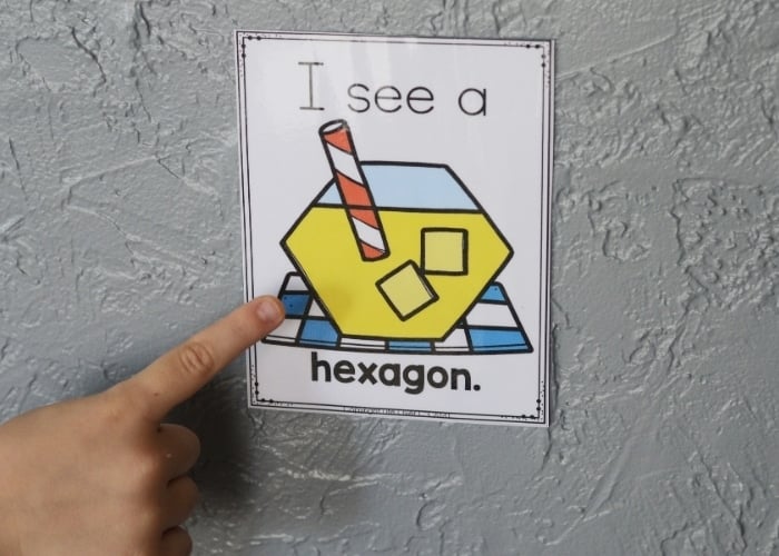 a child pointing to the "i see a hexagon" printable from the lemonade theme free printable 2d shape posters.