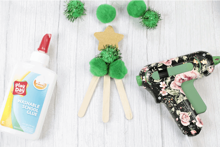 green pompoms being glued onto popsicle sticks to create a christmas tree craft.