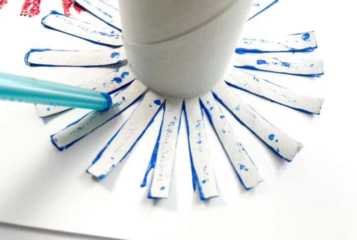 to make the firework art for kids, press the painted toilet paper tube strips onto a blank piece of paper.