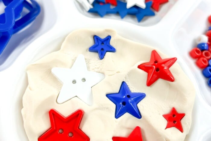 red, white, and blue star-shaped buttons are pressed into a circle of white play dough.