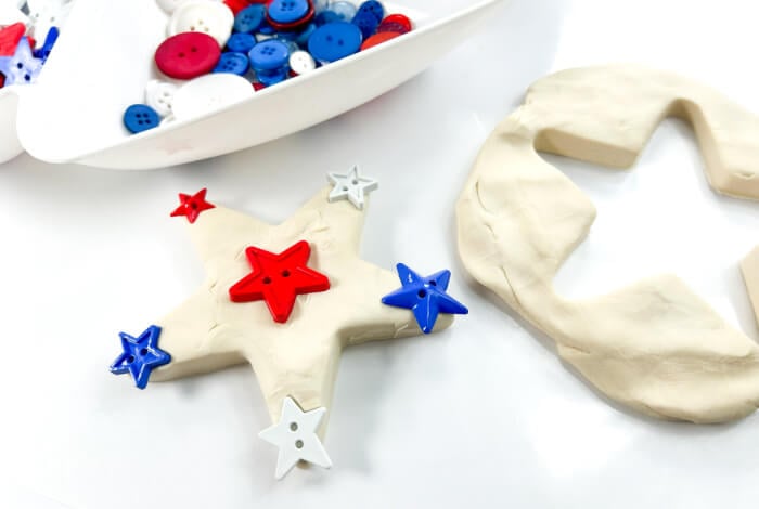 a play dough star is decorated with red, white, and blue star-shaped buttons.
