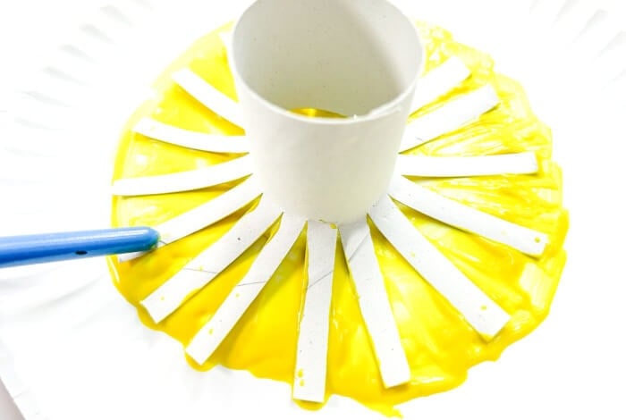 someone is pressing the fringed end of a toilet paper tube into yellow paint.