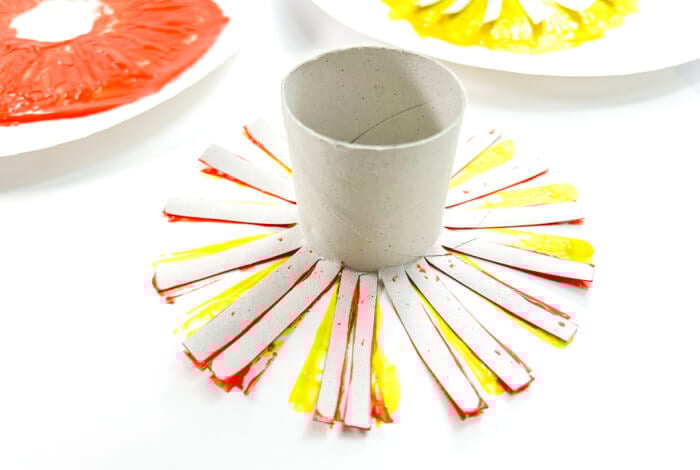 someone is using a toilet paper tube with orange paint to make a sun shape on a piece of paper.