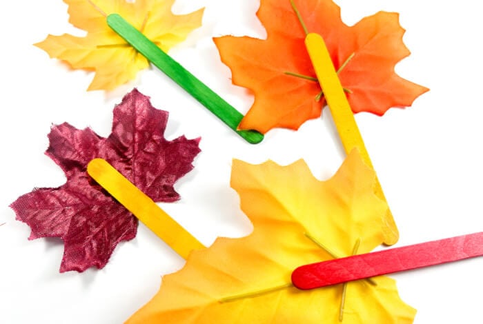 someone is attaching colorful popsicle sticks to the back of faux fall leaves.