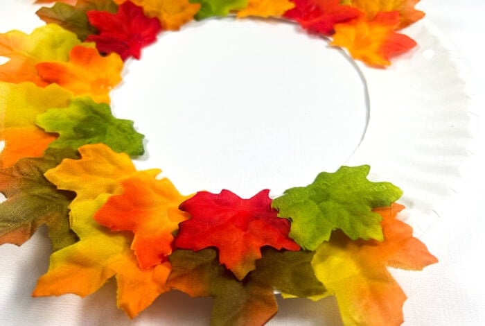 someone is filling up a paper plate wreath with colorful leaves.