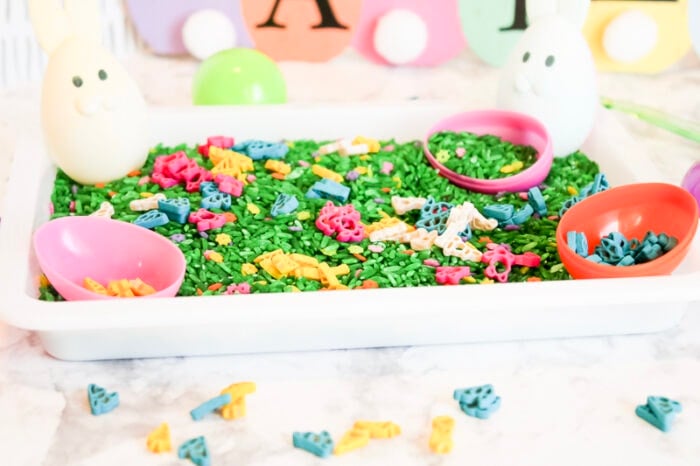 the completed easter sensory bin filled with green rice, painted bunny noodles, and plastic easter eggs.
