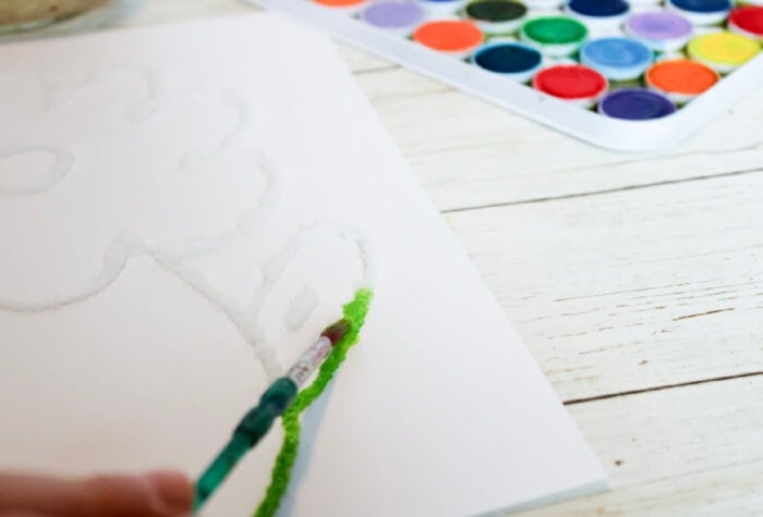 Spring Flower Salt Painting for Kids 20 someone is using a paintbrush and green watercolor to paint a leaf on salt painting flower.