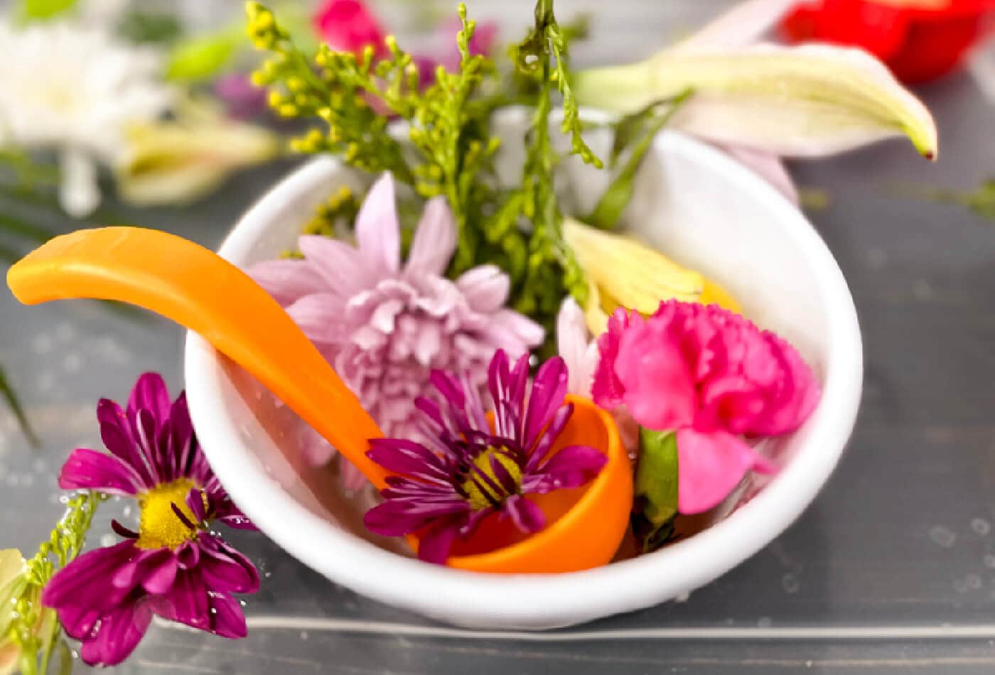 orange toy ladle in white bowl filled with water and pink flower heads for flower soup sensory bin