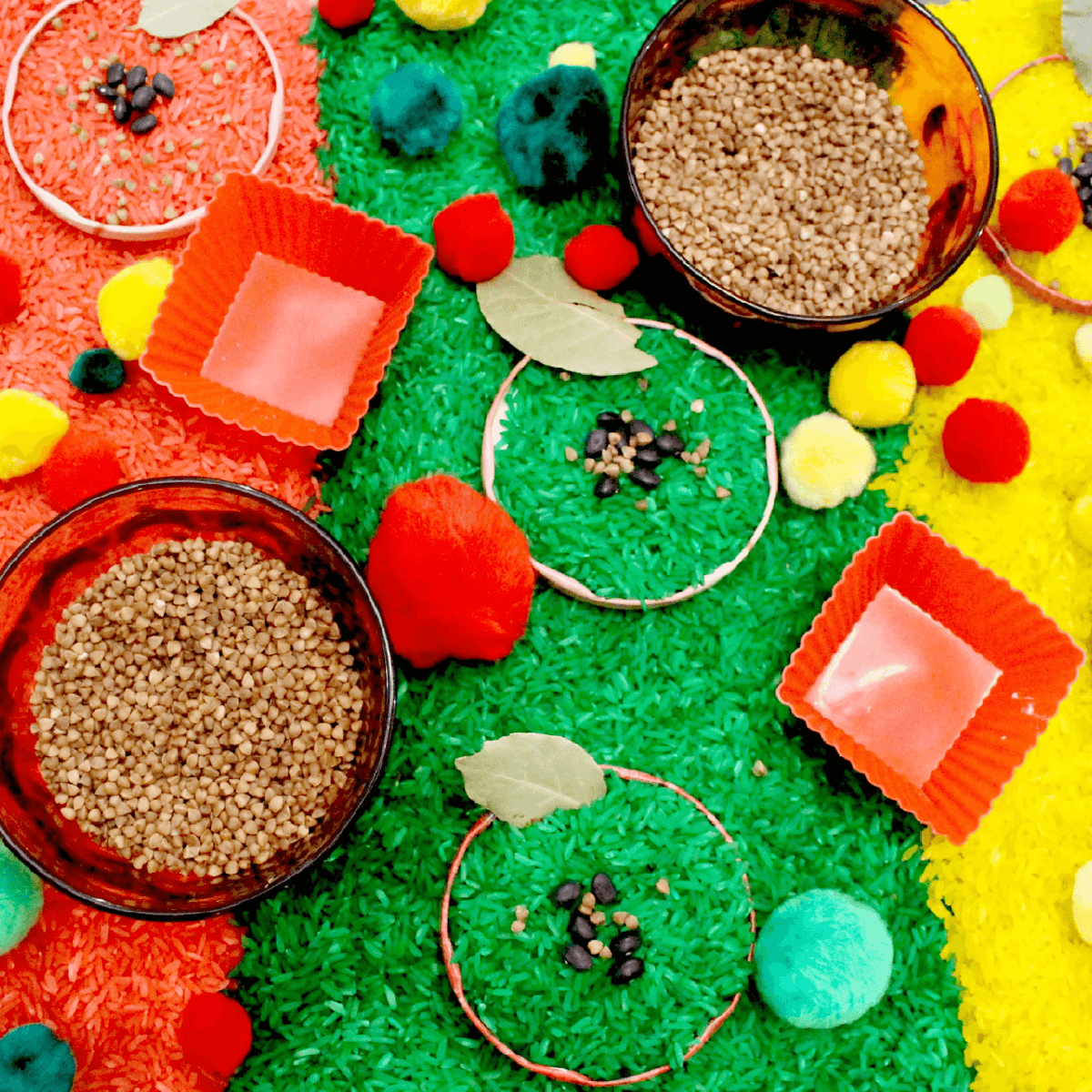 apple theme sensory bin with red, green and yellow dyed rice, bulgar and pom poms