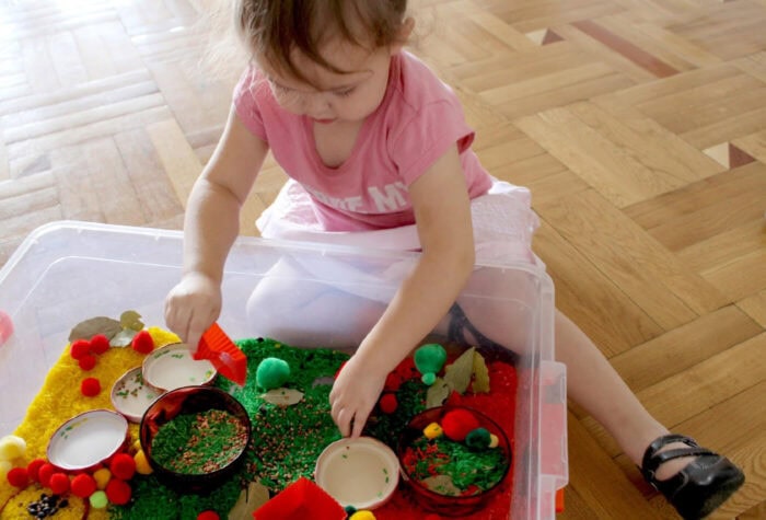 a little girl is playing with rice inside an apple theme sensory bin.