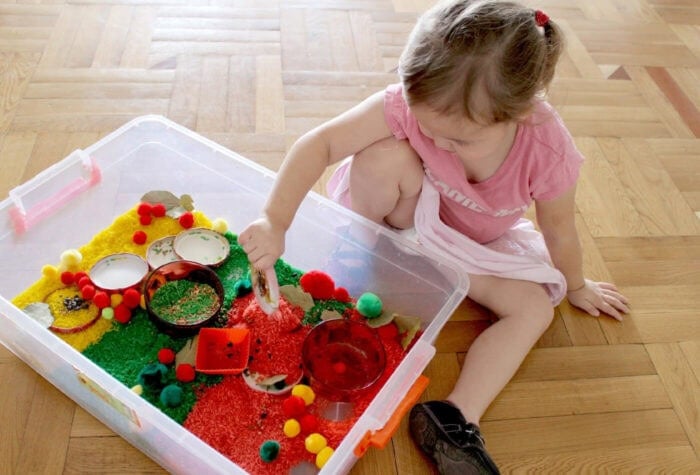 a child is sitting on the floor to play with an apple sensory bin.