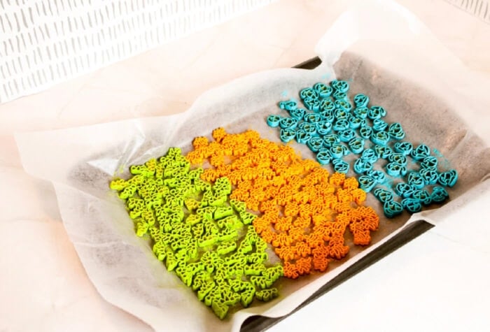 three colors of dinosaur pasta are drying on a cookie sheet.