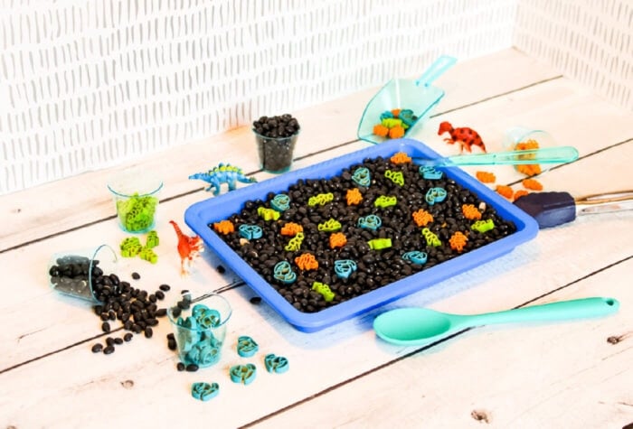 a dinosaur sensory bin made with painted pasta, black beans, and dinosaur toys.