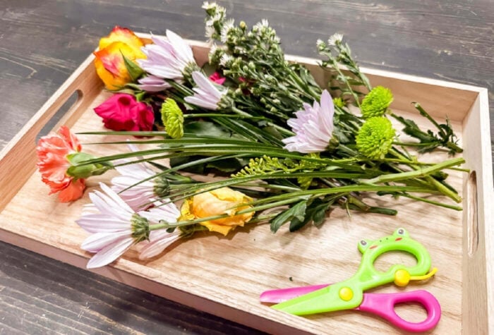a pair of scissors and a bunch of uncut flowers in a wooden tray.