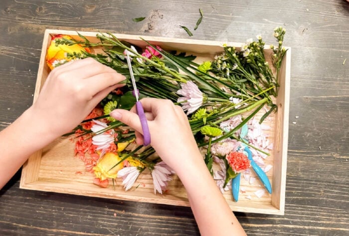 a child using scissors to cut flower stems in a spring sensory bin.