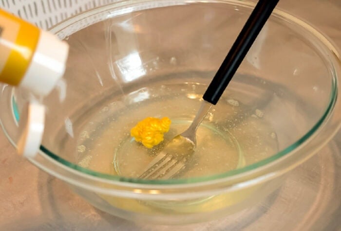 someone is adding gold paint to a clear liquid mixture in a glass bowl.