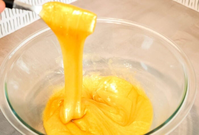 using a fork to stretch golden slime out of a glass bowl.