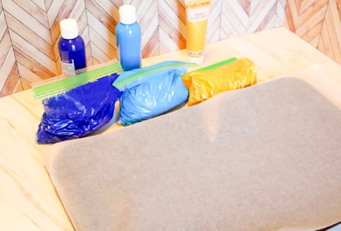 three bags of painted chickpeas are sitting next to a cookie sheet covered in wax paper.