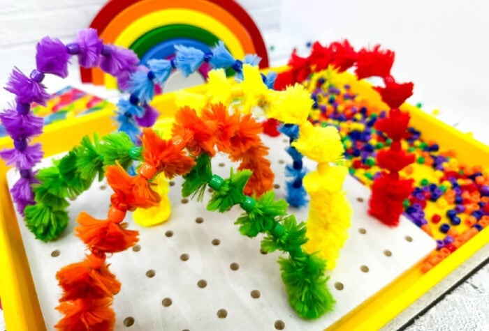 rainbow colored pipe cleaners stuck in various holes across the pegboard to create a design.