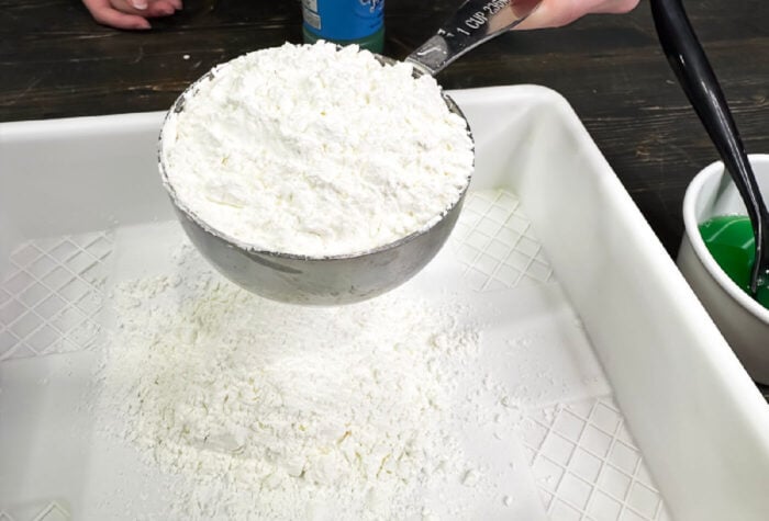 How to Make Spring Flower Ooblek for Kids 16 overhead shot showing cornstarch in a measuring cup over top of a white tray with cornstarch.