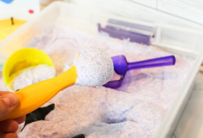 someone is using a spoon to scoop up some of the foam sand from the ocean sensory bin.