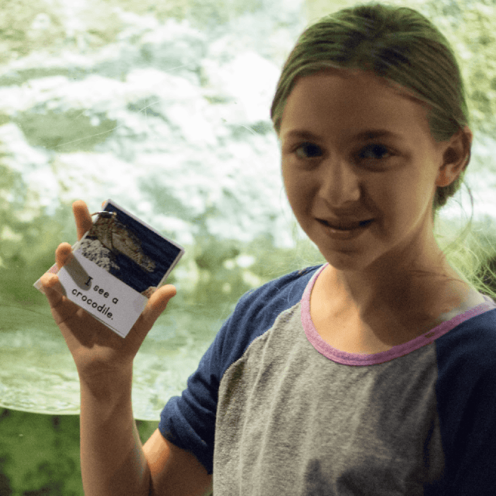 Free Printable Zoo Scavenger Hunt Book for Kids 7 photo of a girl at the zoo holding up a free printable zoo animal scavenger hunt book.