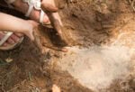 a child's hands are covered in mud while playing with a river sensory bin.
