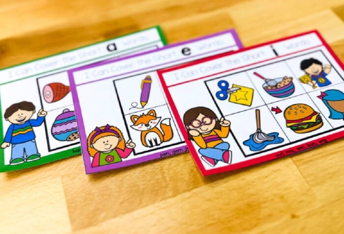 three cvc word task cards on a butcher block counter. text on the task cards says [i can cover the short i words]