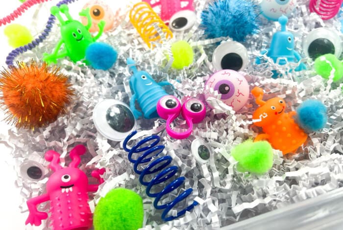monster toys and accessories are in a bin with white shredded paper.