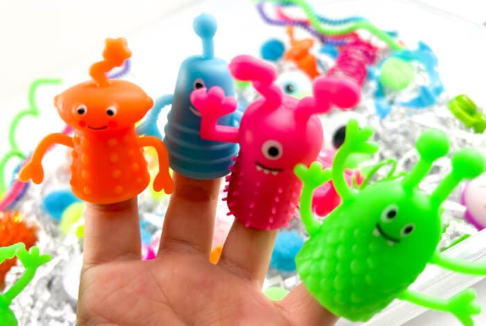 four colorful monster finger puppets are on someone's fingers.