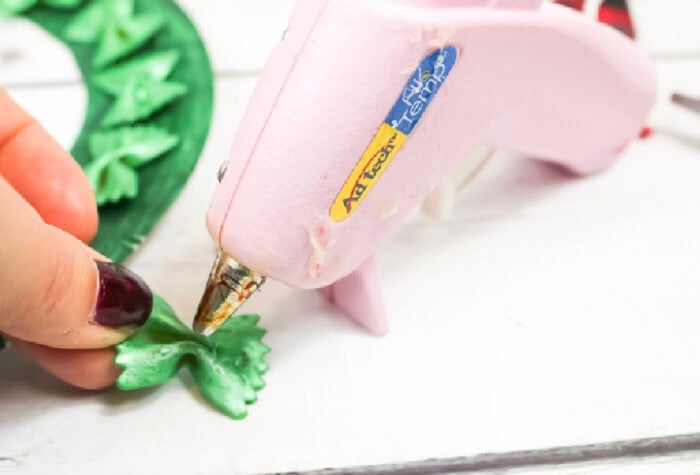photo of pink hot glue gun being used to attached green painted pasta to a christmas paper plate wreath