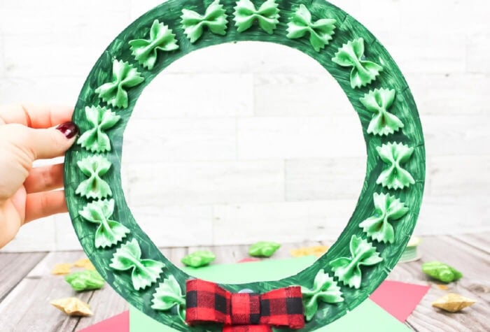 photo of green painted paper plate wreath with green painted farfalle pasta and a red and black buffalo checked bow