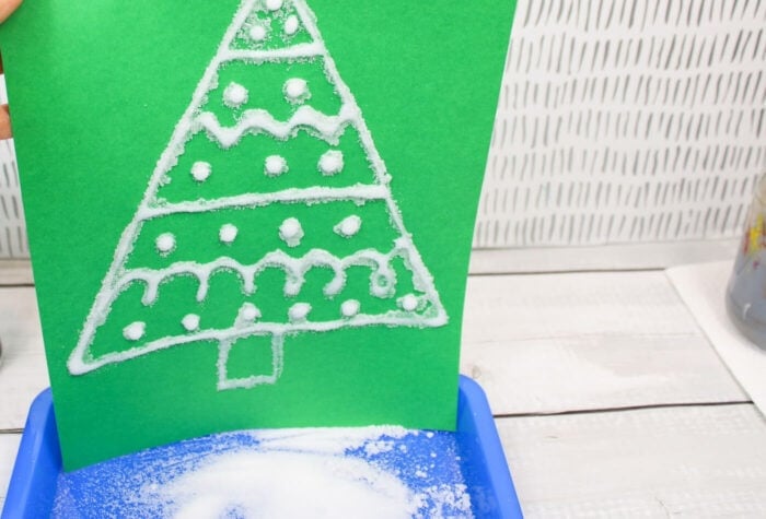 someone is shaking excess salt from a christmas tree salt painting onto a tray.