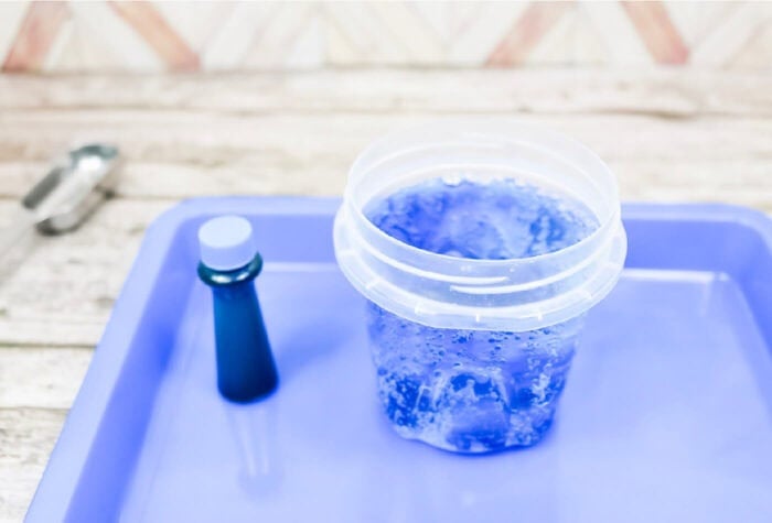adding blue food coloring to club soda in a cup on a blue tray