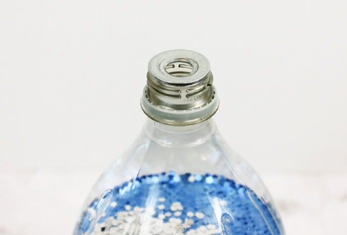 placing a metal washer on the top of a 2-liter bottle for the tornado in a bottle science experiment