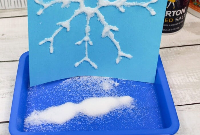 Easy Winter Salt Painting Art Activity for Kids 16 excess salt from a snowflake salt painting is falling into a tray.
