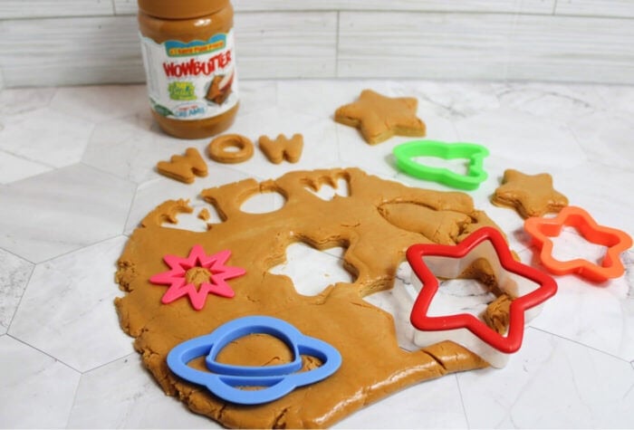 peanut-free edible play dough spread out on a tabletop with colorful shape cutters, made with wow butter for preschool sensory play and fine motor learning.