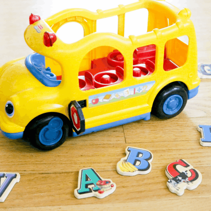 transportation theme activities for preschool and kindergarten featuring a yellow toy school bus surrounded by colorful alphabet letter pieces for hands-on learning.